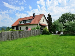 Een huis met een rood pannendak, een houten omheining en een gazon.