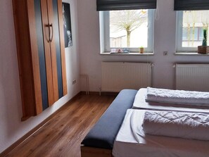 Ein Schlafzimmer mit Bett, Schrank, Fenster und Heizkörper.