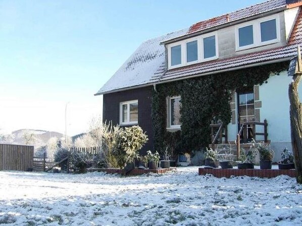 A house with a dark exterior, a tiled roof, and a covered porch with potted plants.