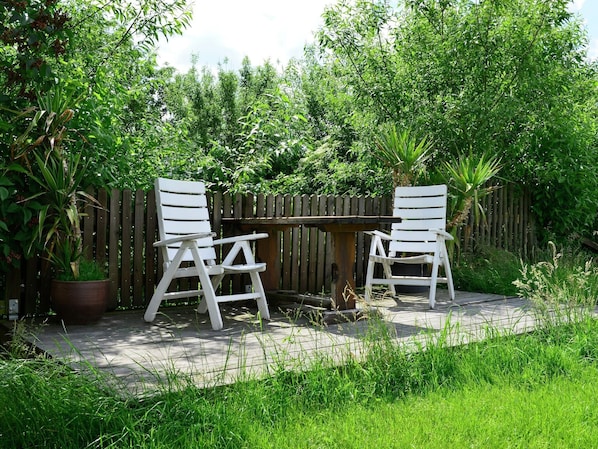 Deux chaises blanches et une table en bois, le tout installé dans un jardin.