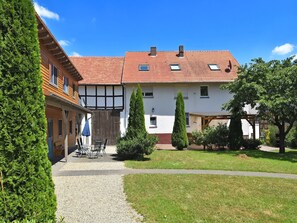 Un bâtiment de style européen traditionnel, avec un toit recouvert de tuiles rouges, un espace extérieur abrité avec des sièges et une pelouse bien entretenue.