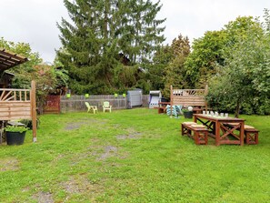 Ein Garten mit Holztisch und Stühlen, einer Holzpergola und einem eingezäunten Bereich mit einem Baum.