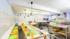 A spacious kitchen with a long wooden table, stainless steel appliances, and various utensils hanging on the wall. - hundefreundliches Gruppenhaus in Hessen mit Garten (Bad Zwesten-Wenzigerode)