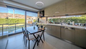 A modern kitchen with a glass dining table and chairs, a dishwasher, and a view of a green landscape.