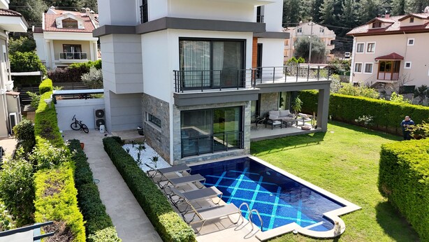 A modern two-story house with a swimming pool, a balcony, and a well-maintained garden.