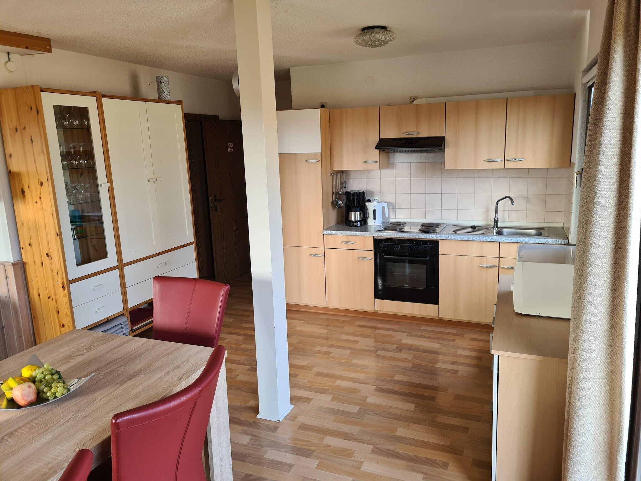 Une cuisine compacte avec des meubles en bois, un four encastré et un coin repas comprenant une table et des chaises.