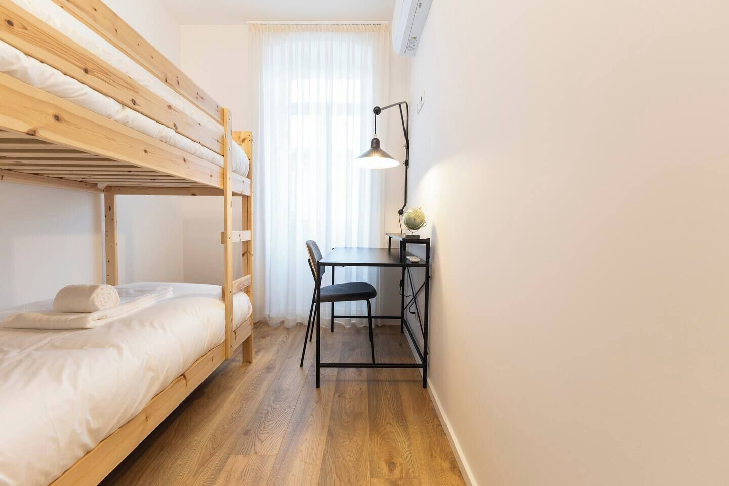 A dorm-style room with a bunk bed, a desk with a chair, and a lamp.