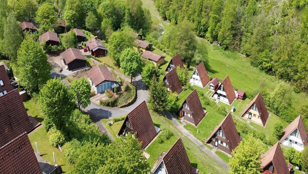 Een woonwijk met huizen met hellende daken, omgeven door weelderige begroeiing en een glooiend landschap.