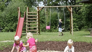 Children playing in a sandy play area with a wooden swing set and a red slide. - Holiday Home in Germany with Scenic Nature (Ronshausen)