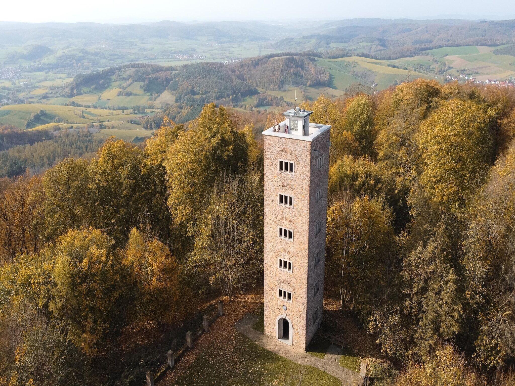 Una torre in pietra con tetto piano, circondata da foglie autunnali.