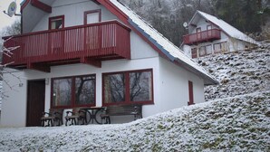 A two-story building with a red balcony, large windows, and a snow-covered hill in the background. - Holiday home in Reimboldshausen with balcony (Kirchheim/Seepark)