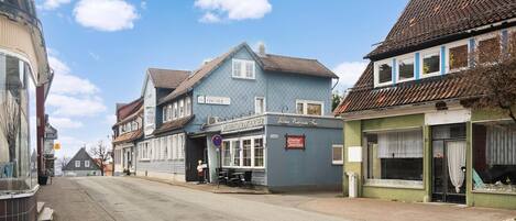 A street view with a blue building labeled 'FISCHER' and a green building with a sign 'Jägermeister'.