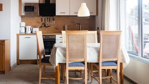 Et moderne køkken med hvide skabe, en mikrobølgeovn og komfur. Der er et spisebord med fire stole, og en hængende lampe over bordet.