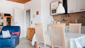 En moderne stue med en blå lædersofa, et spisebord med fire stole og et køkkenområde med træskabe og en hængende lampe.