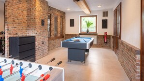 A room with a pool table, foosball table, brick walls, and a window with a view. - Holiday home with sauna in the Eifel National Park (Schleiden)