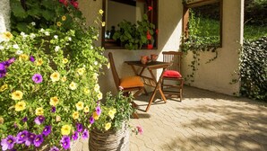 En terrasse med et bord og stole, omgivet af krukker med planter og blomster.