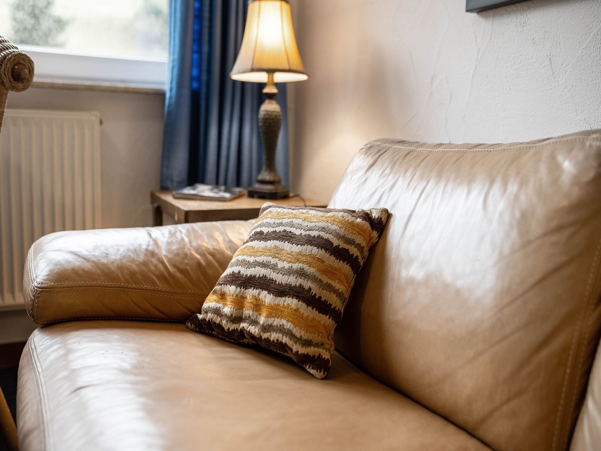 Un canapé en cuir agrémenté d’un coussin à motifs, une lampe de table et une fenêtre avec des rideaux.