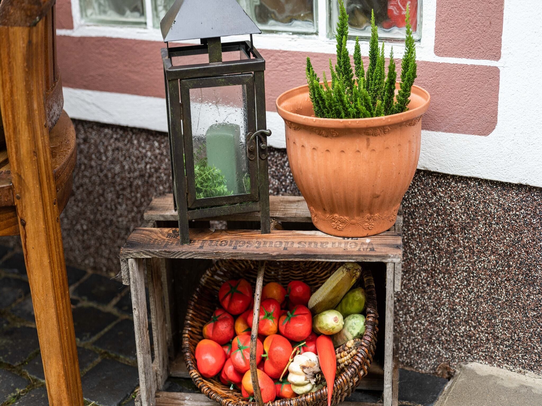 Ein Laterne, ein Blumentopf und ein Korb voller Gemüse auf einer Holzkiste.