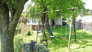 A playground with swings and a slide, surrounded by a well-maintained lawn and flowering plants.