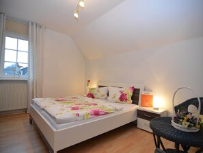 A bedroom with a bed, a nightstand, a chair, and a window with curtains.