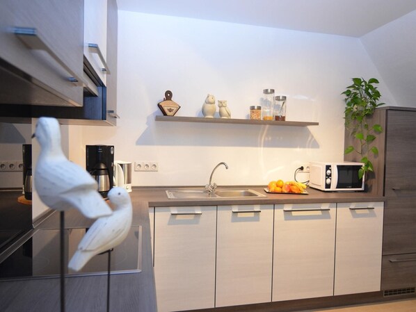 A modern kitchen with a built-in dishwasher, a microwave, and a sink. There are decorative items on a shelf above the sink, including a small owl figurine and a vase. - Ferienwohnung in Wehrstapel (Meschede)