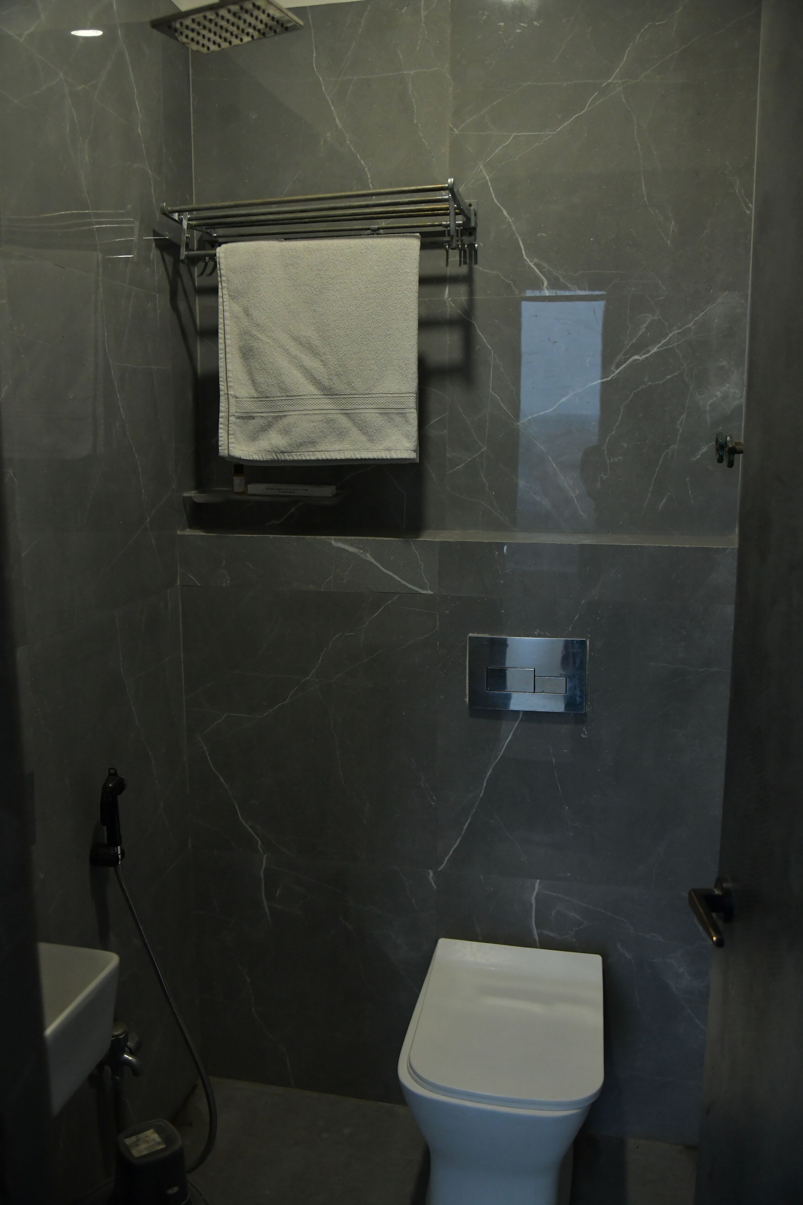 Un baño moderno con pared de mármol, inodoro blanco, barra para toallas y cabezal de ducha.