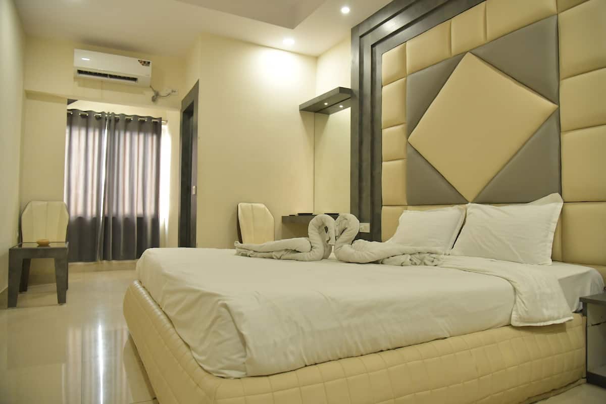 A hotel room with a large bed, a bedside table, a chair, and a window with curtains.