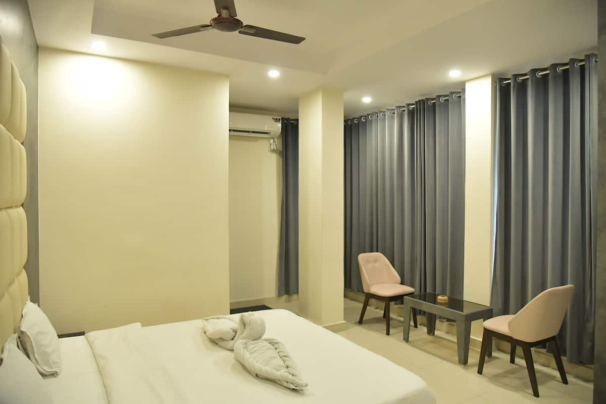 A hotel room with a bed, a chair, a small table, a ceiling fan, and curtains.