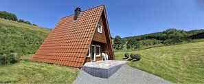 Ett litet, trekantigt trähus med ett sluttande tak, en ytterdörr och en liten veranda.
