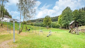 A park with a playground, a wooden structure, and a house in the background. - Charmantes Ferienhaus in Skigebietsnähe (Bestwig-Untervalme)
