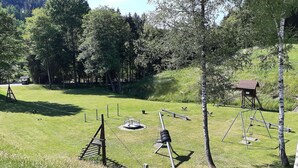 A grassy outdoor area with exercise equipment, a small wooden structure, and trees. - Charmantes Ferienhaus in Skigebietsnähe (Bestwig-Untervalme)