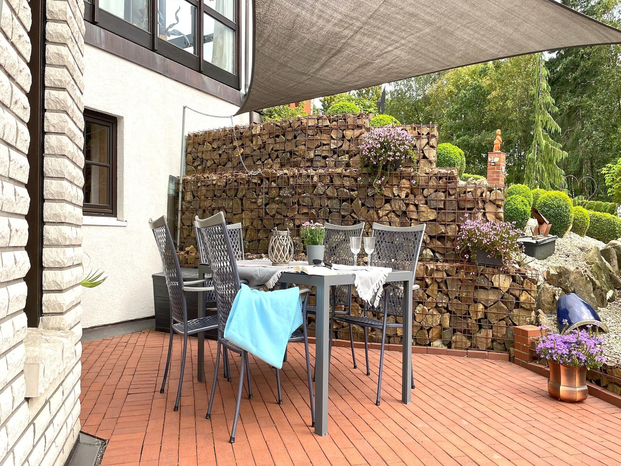 Un patio al aire libre con una mesa y sillas, un muro de piedra y una estatua.
