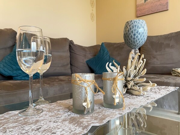 A living room with a glass coffee table, two wine glasses, and decorative items on a lace tablecloth.