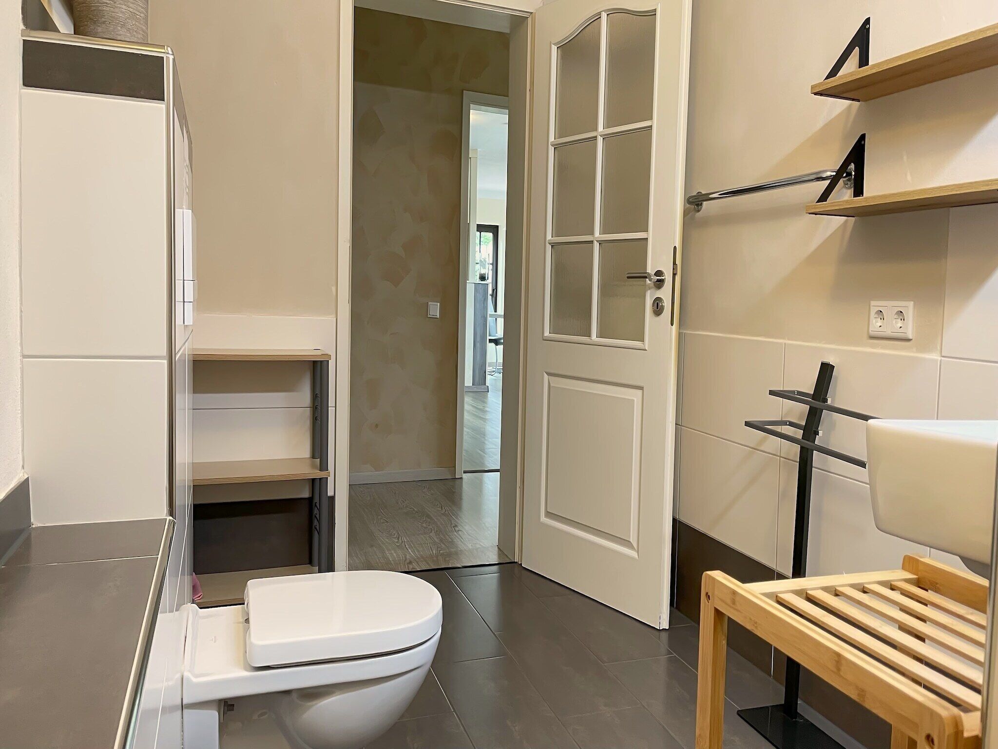 A modern bathroom with a toilet, a shower area, and a wooden bench.