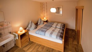 A bedroom with a wooden bed, a bedside table with a lamp, a wooden wardrobe, and a bathroom with a sink and towel rack.
