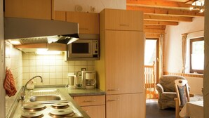 A compact kitchen with a microwave, coffee maker, and stove. There is a dining area with a chair and table.