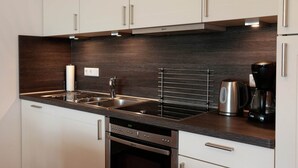 Eine moderne Küche mit weißen Schränken, Edelstahlgeräten und einer dunklen Holzrückwand.