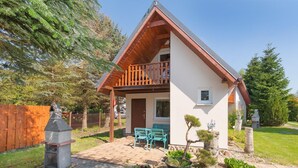 A two-story house with a wooden balcony, a brick patio, and a small garden area. - Spacious and Comfortable Holiday Homes With Pool (Darlowo)