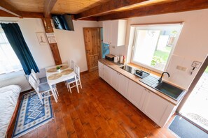 A compact kitchen with a wooden floor, white cabinets, a dining table with chairs, a window with a view, and a built-in sink.