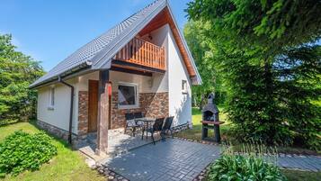 Una casa de dos pisos con balcón, chimenea de ladrillo y patio empedrado.