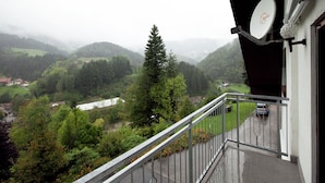 Un balcon donnant sur une vallée, une antenne parabolique et une voiture garée à l’extérieur.