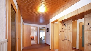 Un couloir aux murs et au plafond en bois, recouvert d’un tapis à motifs, et une porte donnant sur une pièce où se trouvent un lit et une chaise.