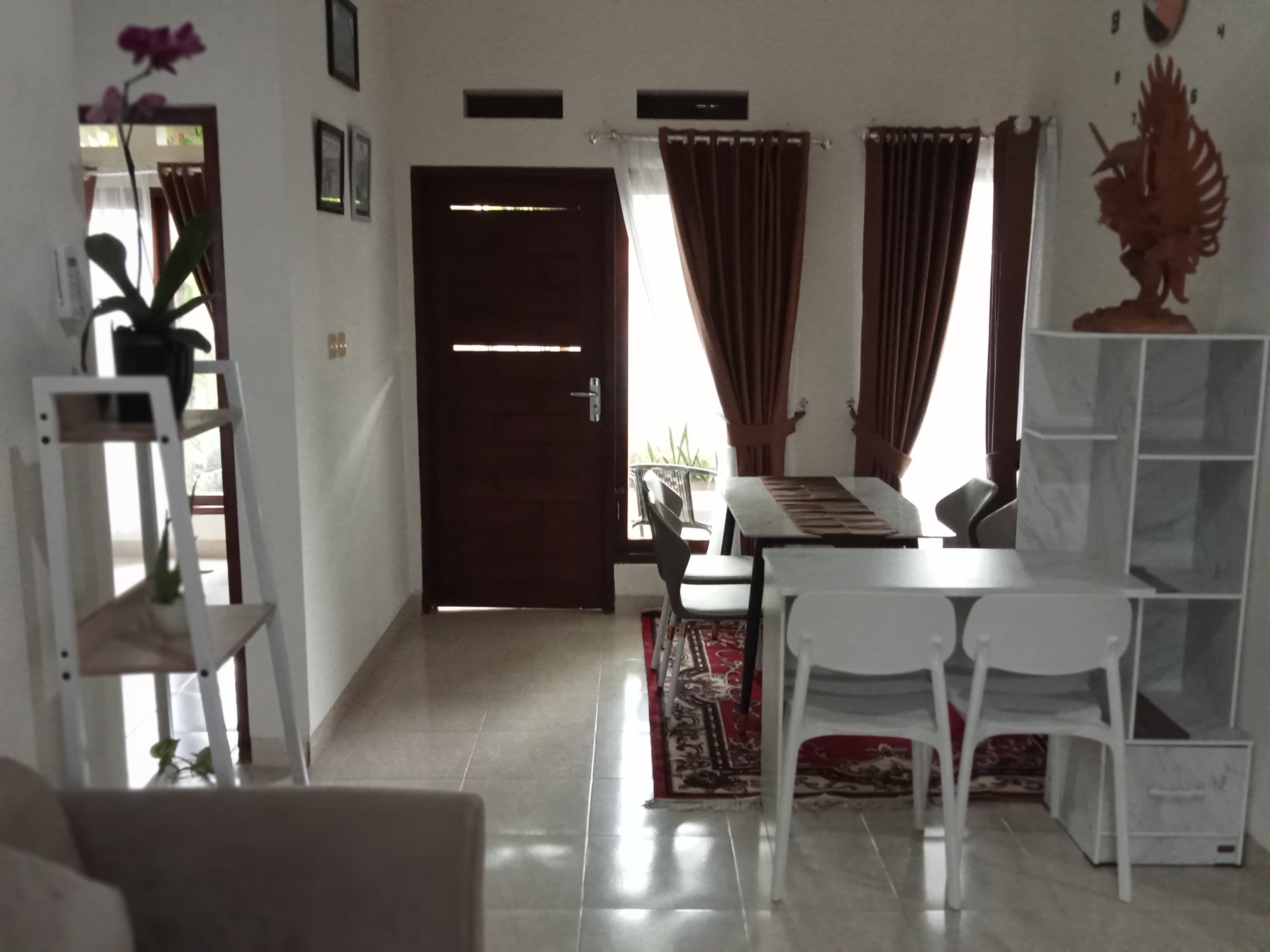 A living room with a dark wooden door, white chairs, a small table, and a decorative plant.
