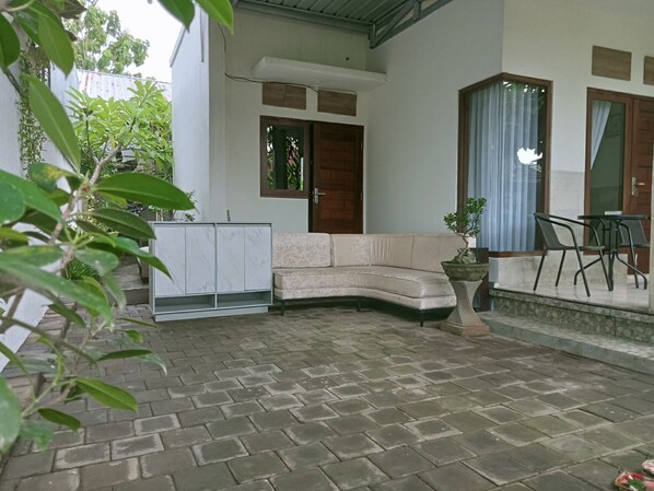 A curved sofa, a small table with chairs, and a potted plant in a courtyard with a tiled floor.