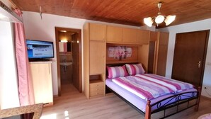 Ein Schlafzimmer mit Holzboden, einem Bett mit gestreifter Bettdecke, einem Holzschrank und einem Fernseher auf einem Schreibtisch.