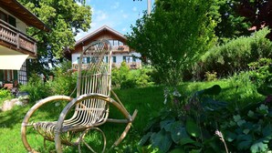 Ein Schaukelstuhl aus Bambus in einem üppigen Garten, im Hintergrund ein Gebäude.