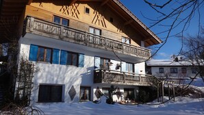 Eine zweistöckige Chalet mit hölzernen Balkonen und einem verschneiten Gelände.