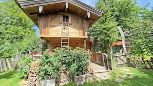 Eine hölzerne Konstruktion mit Kreuz darauf, eine Holztreppe und ein Garten mit Pflanzen und Blumen.