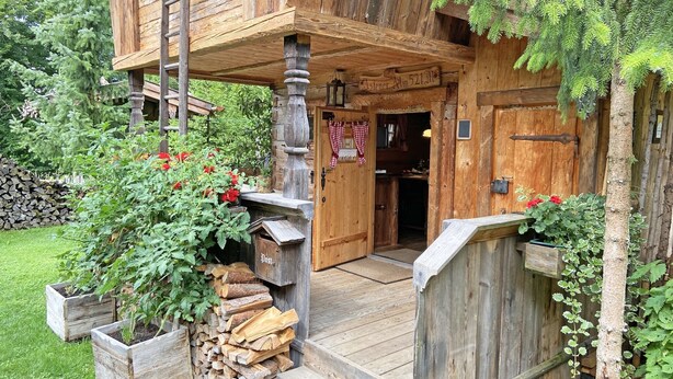 A rustic wooden building with a lofted upper level, a wooden staircase, and a door with a red and white checkered curtain. - Bayerisches Refugium mit Sauna (Tittmoning)