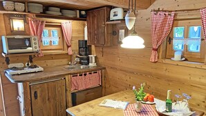 A cozy kitchen with wooden walls, a wooden table, a sink, a microwave, and a coffee maker. - Bayerisches Refugium mit Sauna (Tittmoning)